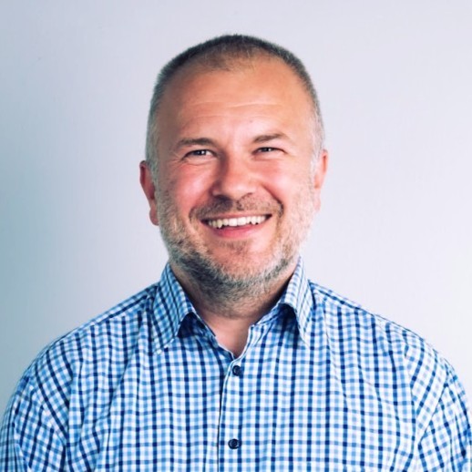 Professional headshot of a male enterprise sales director in a tailored navy suit, confident friendly smile, modern corporate office background, professional lighting